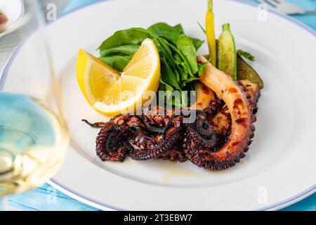 Polpo grigliato con rucola e mini verdure su un piatto di porcellana bianca Foto Stock