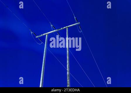 cielo notturno blu con linee elettriche su vecchi pali di legno Foto Stock