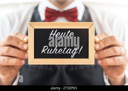 25 ottobre 2023: Cameriere tiene in mano una tavoletta con l'iscrizione: Today of Rest PHOTOMONTAGE *** Kellner hält eine Tafel in der Hand mit Aufschrift: Heute Ruhetag FOTOMONTAGE Credit: Imago/Alamy Live News Foto Stock