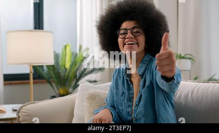 Felice sorriso eccitato vincitore afro-americano donna padrona di casa ragazza acquirente cliente raggiungere casalinga sorriso sorriso guardare positivo fotocamera mostra pollice Foto Stock