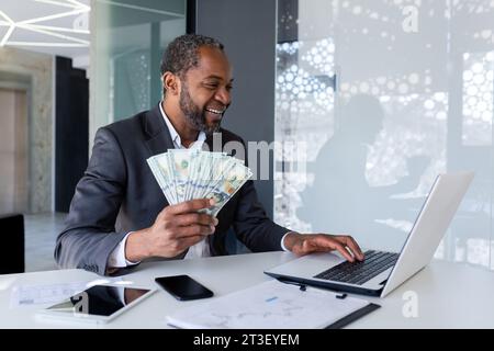 L'uomo d'affari Joyful ha ottenuto un reddito da guadagno, l'uomo conta denaro in dollari americani in contanti in ufficio sul posto di lavoro, il capo di successo soddisfatto dei risultati raggiunti, il banchiere finanziario in tuta aziendale. Foto Stock