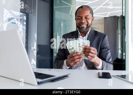 L'uomo d'affari Joyful ha ottenuto un reddito da guadagno, l'uomo conta denaro in dollari americani in contanti in ufficio sul posto di lavoro, il capo di successo soddisfatto dei risultati raggiunti, il banchiere finanziario in tuta aziendale. Foto Stock