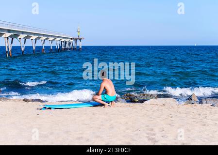 Un giovane serio che pulisce la tavola da surf sulla spiaggia soleggiata Foto Stock