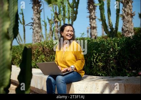 Sorridente giovane adulto multietnico Happy Woman, uno studente laureato all'università che guarda da parte mentre studia online utilizzando un notebook. Persone, stile di vita, e Foto Stock