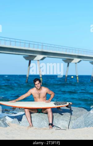 Un giovane serio che pulisce la tavola da surf sulla spiaggia soleggiata Foto Stock