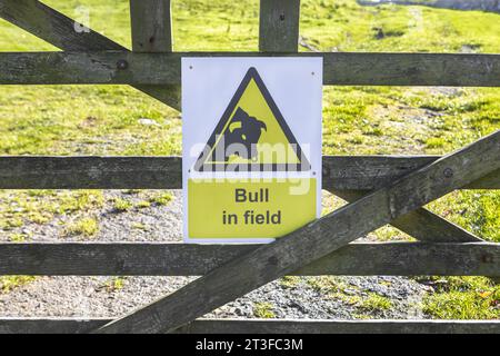 Un cartello su un cancello a cinque barre che avverte del toro nel campo Foto Stock