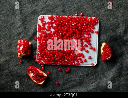 Maturare i semi di melograno su un piatto su sfondo nero Foto Stock