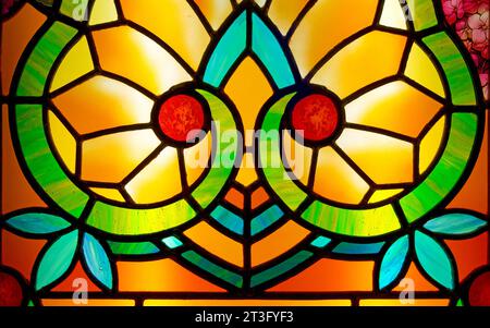 Piccolo dettaglio di una generica vetrata in stile Art Nouveau. Toni giallo arancio e rosso, con note floreali blu e verde. Foto Stock