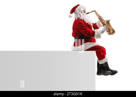 Foto del profilo di Babbo natale seduto su un muro e che suona un sassofono isolato su sfondo bianco Foto Stock