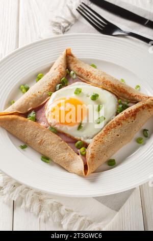 Crepe galette di grano saraceno fatta in casa con primo piano di uova, prosciutto e cipolla verde sul piatto sul tavolo. Verticale Foto Stock