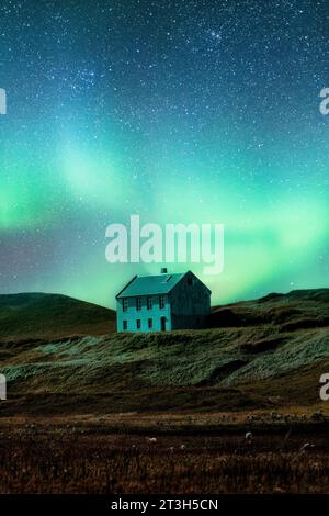 Fantastico panorama dell'aurora boreale o dell'aurora boreale che brilla sopra la casa scandinava abbandonata su una collina in una posizione remota la notte in Islanda Foto Stock