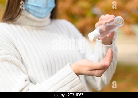 Donna con maschera di protezione medica che mette su antisettico per disinfettare le mani Foto Stock