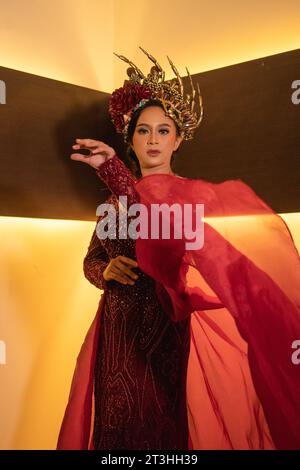 Una bella donna asiatica alza la coda di tessuto rosso indossando un abito da sposa rosso prima della cerimonia di nozze Foto Stock