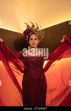 Una bella donna asiatica alza la coda di tessuto rosso indossando un abito da sposa rosso prima della cerimonia di nozze Foto Stock