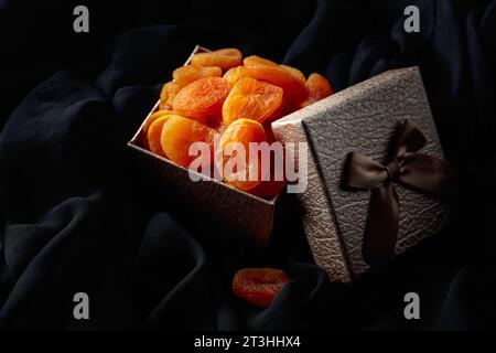 Albicocche secche in una scatola regalo su un panno nero. Foto Stock