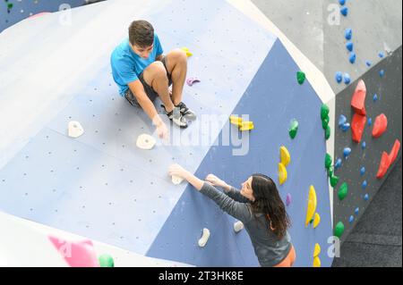 Un paio di atleti che si muovono su una roccia ripida, arrampicano su una parete artificiale al chiuso. Sport estremi e concetto di Boulder Foto Stock