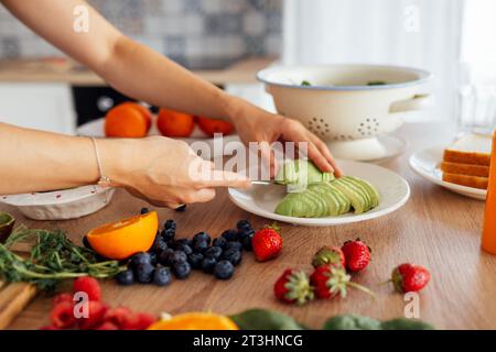 Una bella donna asiatica sorride e cucina la colazione in cucina. Una giovane affascinante donna coreana ride e taglia verdure e pesce. Sana f Foto Stock