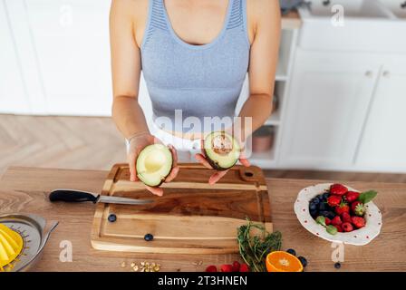 Una bella donna asiatica sorride e cucina la colazione in cucina. Una giovane affascinante donna coreana ride e taglia verdure e pesce. Sana f Foto Stock