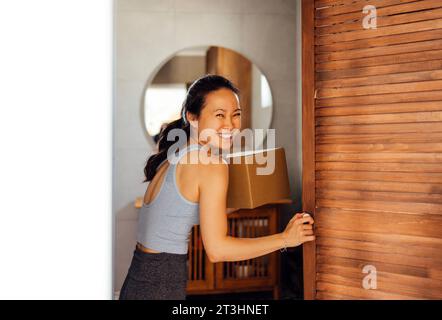 Bella giovane donna asiatica prende scatola di cartone fuori dall'armadio. Una donna coreana sorridente in abiti informali con pacchetto nel corridoio della casa. Attracti Foto Stock