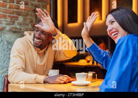 Allegra giovane coppia di mezza età. Amici afro-americani e donne caucasiche che salutano il loro nuovo amico mentre si siede e si fa beffe Foto Stock