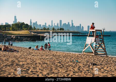 Un bagnino siede di guardia a Oakwood Beach, sul lago Michigan, Chicago. Lo skyline della città fa da sfondo Foto Stock