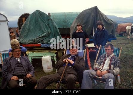 Gruppo di famiglia Gypsy, Appleby nel Westmorland, fiera dei cavalli gitani in Cumbria. Un gruppo di zingari siede intorno al fuoco del campo e passa l'ora del giorno. Le loro tradizionali roulotte in legno con tetto a prua sono sullo sfondo. Inghilterra Regno Unito giugno 1985 1980s UK Charter Fair concessa da re Giacomo II 1685 HOMER SYKES Foto Stock