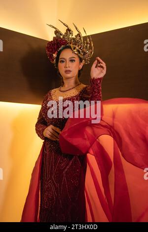 Una bella donna asiatica alza la coda di tessuto rosso indossando un abito da sposa rosso prima della cerimonia di nozze Foto Stock