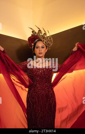 Una bella donna asiatica alza la coda di tessuto rosso indossando un abito da sposa rosso prima della cerimonia di nozze Foto Stock
