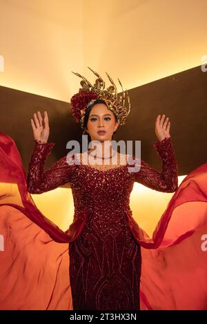 Una bella donna asiatica alza la coda di tessuto rosso indossando un abito da sposa rosso prima della cerimonia di nozze Foto Stock