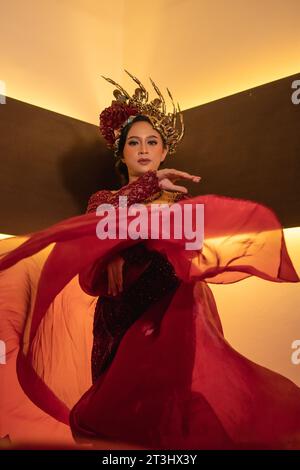 Una bella donna asiatica alza la coda di tessuto rosso indossando un abito da sposa rosso prima della cerimonia di nozze Foto Stock
