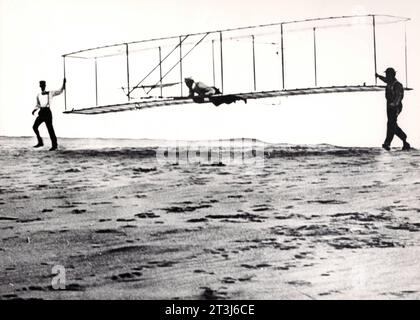 Il terzo aliante di prova dei fratelli Wright fu lanciato a Kill Devil Hills, North Carolina, il 10 ottobre 1902. Wilbur Wright è ai comandi, Orville Wright è a sinistra, e Dan Tate (un residente locale e amico dei fratelli Wright) è a destra. I 1902 alianti di prova furono estremamente importanti per lo sviluppo del primo aereo motorizzato. Il nuovo progetto di aliante si basava sui test della galleria del vento eseguiti dalla Wrights nel 1901. I miglioramenti all'aliante includevano un nuovo timone che aiutava a fornire il controllo tridimensionale dell'aereo. Foto Stock