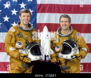 STS-2 prime Crew, composto dal comandante Joe Engle e dal pilota Richard, in piedi di fronte a una bandiera americana che regge i caschi con un modello Shuttle sul tavolo davanti a loro. Foto Stock