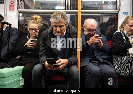 I pendolari della South Western Rail si arrampicavano sui posti a sedere che navigavano sui loro smartphone durante l'ora di punta su un treno dalla stazione principale di Waterloo di Londra. Foto Stock