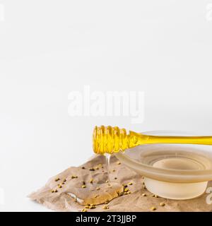 Avvicinare il miele dolce che gocciola dal cucchiaio con la carta marrone dei semi di polline delle api Foto Stock