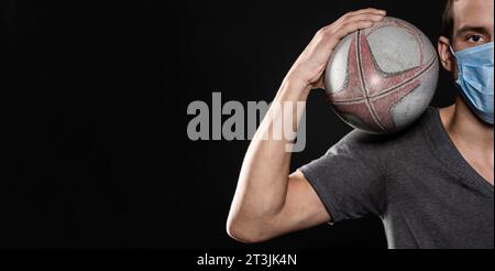 Vista frontale giocatore di rugby maschile con palla maschera medica Foto Stock
