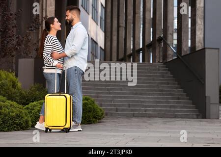 Relazione a distanza. Bella coppia giovane con valigia vicino a un edificio all'aperto Foto Stock