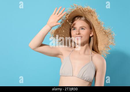 Bella giovane donna con cappello di paglia che si ombreggiava con la mano dalla luce del sole su sfondo azzurro. Spazio per il testo Foto Stock