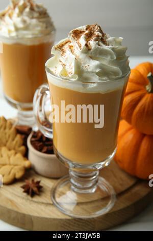 Gustoso latte di zucca con panna montata nei bicchieri, spezie e biscotti sul tavolo bianco, primo piano Foto Stock