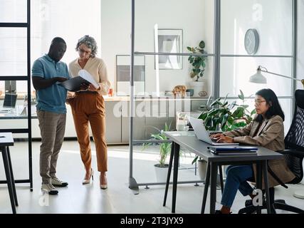 Donna d'affari matura e dipendente afroamericano che discute di documenti mentre si trova al centro della moderna area di coworking Foto Stock