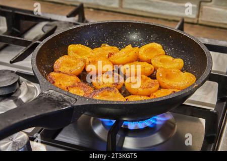 Le metà delle albicocche fresche vengono fritte in sciroppo di caramello in padella sul fornello a gas. Foto Stock