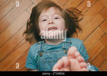 Divertente ritratto al coperto di un ragazzo biondo caucasico che guarda la fotocamera sorridente dall'alto Foto Stock