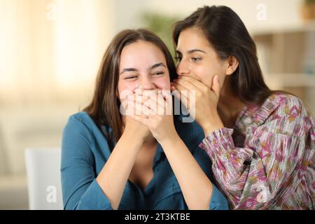 Una donna felice che racconta un segreto divertente alla sua amica a casa Foto Stock