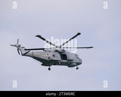 Un elicottero grigio della guardia costiera inglese sorvola con la porta aperta contro un cielo grigio al largo della costa inglese vicino a Falmouth in Inghilterra Foto Stock