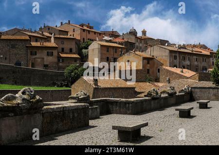 Le effigie senza testa degli antichi Etruschi si adagiano sui coperchi del sarcofago, ora adagiati lungo una bassa parete della piazza a Tuscania, Lazio, Italia. Il centro storico di Tuscania sorge alle spalle. Tuscania era un tempo l'antica città etrusca di Tuscana. Si trova a circa 80 km (50 miglia) a nord-ovest di Roma. Foto Stock