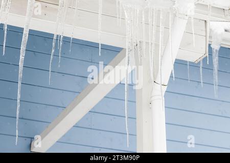 I ghiacci si appendono sul tetto della casa rurale su sfondo blu Foto Stock