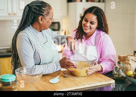 Madre e figlia africana che preparano una torta sana a casa - cottura, concetto di stile di vita familiare - Focus sul viso della mamma Foto Stock