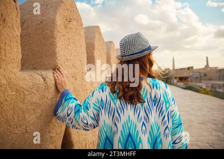 Ritratto di giovane donna in abito etnico con ornamento blu e cappello che cammina alle mura della città di Itchan Kala, antica città di Khiva in Uzbekistan. Foto Stock
