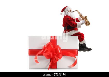 Foto del profilo di Babbo natale seduto su un regalo e che suona un sassofono isolato su sfondo bianco Foto Stock