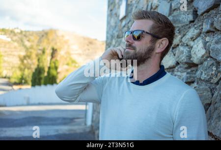 Uomo con smartphone - giovane uomo d'affari che parla con uno smartphone. Uomo d'affari professionista urbano informale che usa il cellulare e sorride una bella passeggiata. Foto Stock