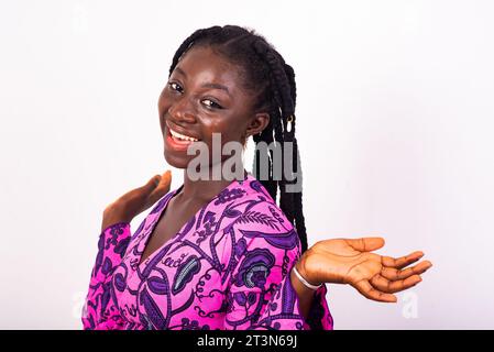 giovane bella donna africana con trecce in piedi su sfondo bianco che guarda la fotocamera con aria entusiasta. Foto Stock